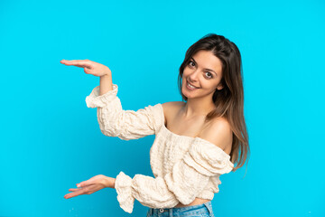 Young caucasian woman isolated on blue background holding copyspace to insert an ad
