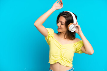 Young caucasian woman isolated on blue background listening music and dancing