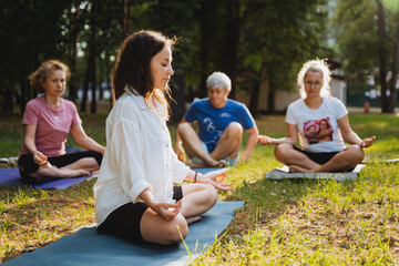 Group meditation, people in the park doing yoga while sitting on mats, yoga instructor doing meditation practice.