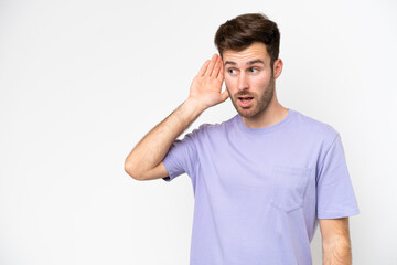 Young caucasian man isolated on white background listening to something by putting hand on the ear