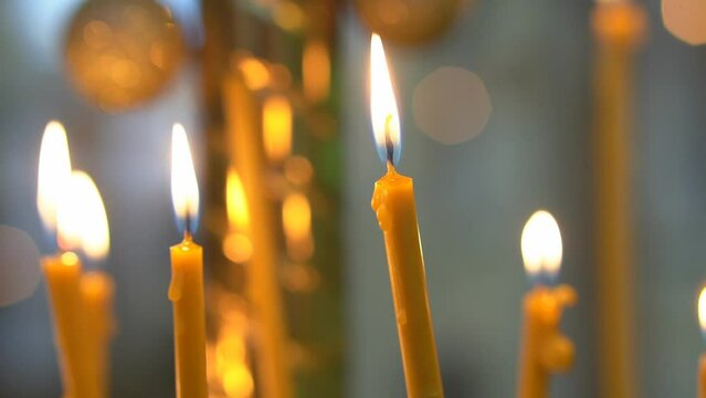Lighting wax candles inserted in sand burning in temple spreading light on blurred background. Worship traditions in Christian church close view