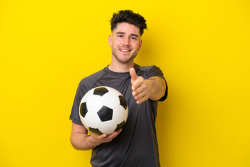 Handsome young football player man isolated on yellow background shaking hands for closing a good...