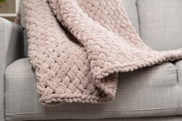 Knitted large plaid blanket in dusty rose light grayish-red color on the sofa.