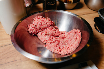 Raw Ground Beef in Stainless Steel Mixing Bowl. Raw ground beef ready for cooking, placed in a shiny metal bowl on a kitchen worktop, surrounded by cooking utensils and equipment.
