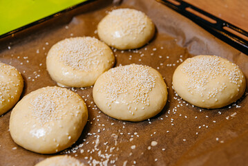 Unbaked Sesame Seed Buns on Baking Tray. Raw dough for buns topped with sesame seeds ready to be baked on a parchment-lined tray.