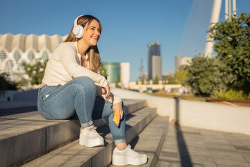 chica joven alegre escuchando música con auriculares por la calle
