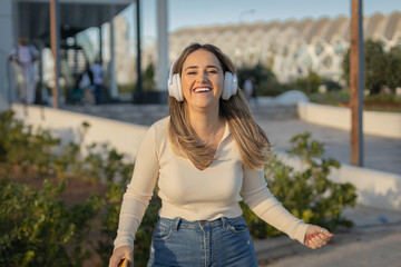 chica joven alegre escuchando música con auriculares por la calle