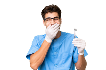 Young dentist man holding tools over isolated background happy and smiling covering mouth with hand