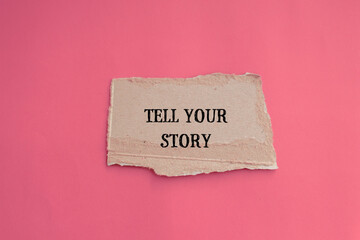 Tell your story lettering on ripped paper piece with pink background. Conceptual photo. Top view,...
