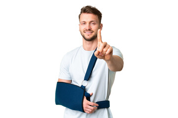 Young caucasian man with broken arm and wearing a sling over isolated chroma key background showing and lifting a finger