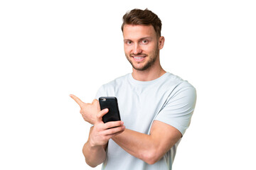 Young handsome caucasian man over isolated chroma key background using mobile phone and pointing back
