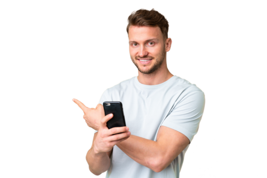 Young handsome caucasian man over isolated chroma key background using mobile phone and pointing back