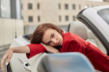Attractive young brunette woman in red blazer sitting with head resting on hand in passenger seat...