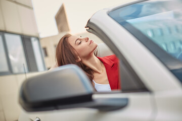 Dreamy young brunette sitting with eyes closed in convertible car