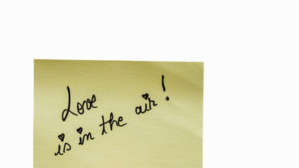 Love is in the air handwriting text close up isolated on yellow paper with copy space.