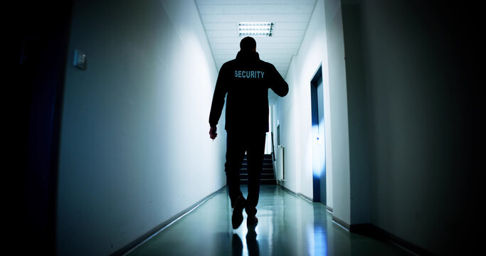 Male Security Guard Holding Flashlight Standing In Corridor