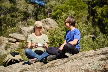 Young mother with kid sitting on stone with stainless tiffin in forest