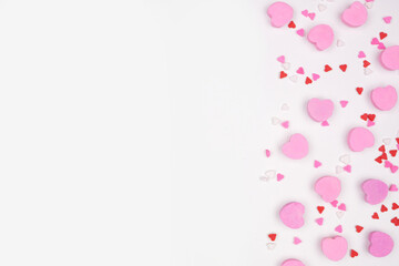 Valentines Day side border of candy hearts and sprinkles. Top view on a white background. Copy...