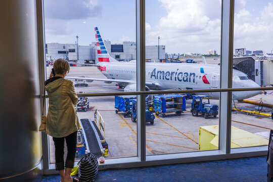 Close-up view of woman talking on mobile phone at the airport with American Airlines plane in the background. Miami. USA. 