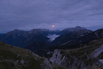 Moon just before setting down shines a radiant glow on the fog in the valley. A view from the Mangart saddle towards the setting full moon. Mangart (2679 m) is a mountain in the Julian Alps.