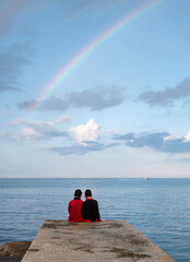 due bambini, di spalle, in riva al mare osservano l'arcobaleno