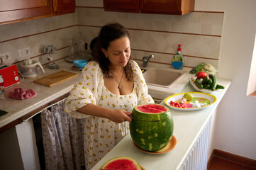 Overhead View of a pleasant housewife cutting ripe organic juicy watermelon in the rustic home kitchen interior