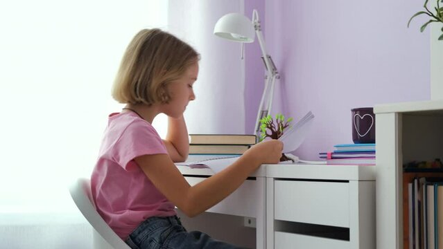 Bored little girl doing homework while sitting at desk. Distance learning and remote education concept