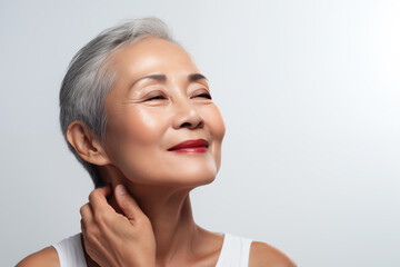 Gorgeous senior older Asian woman with makeup touching her neck and looking at camera