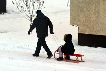 A father pulls a child on a sled in a snowy winter