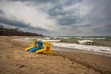 colorful beach chairs blown over by winter storm winds with dramatic breaking surf and blue clouds kew beach toronto room for text