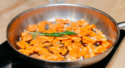 Sauteing Chopped Carrots with Fresh Rosemary in Pan. Chopped carrots being sauteed in a stainless steel pan with fresh rosemary, the start of a flavorful and healthy dish.