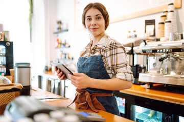 Portrait of a smiling cafe owner using a digital tablet behind the bar counter in a modern coffee...