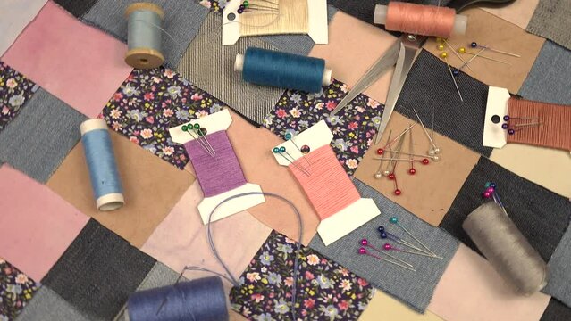 Accessories for patchwork sewing. Needles, tailor's pins, spools of thread, scissors lie on a textile in patchwork style with   printed cotton fabric and denim elements in blue tones