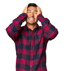 Young Chinese man in studio background laughs joyfully keeping hands on head. Happiness concept.