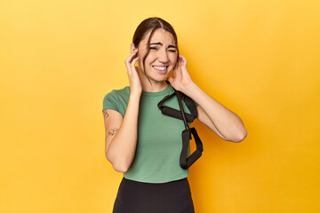 Fitness young woman with resistance bands covering ears with hands.