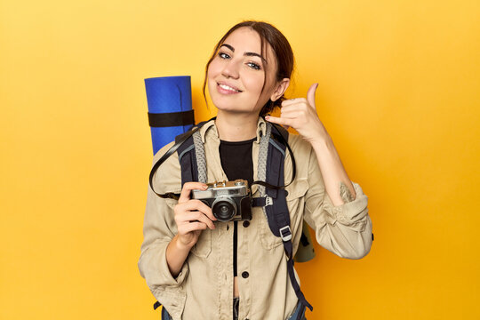 Photographer with gear ready to explore showing a mobile phone call gesture with fingers.