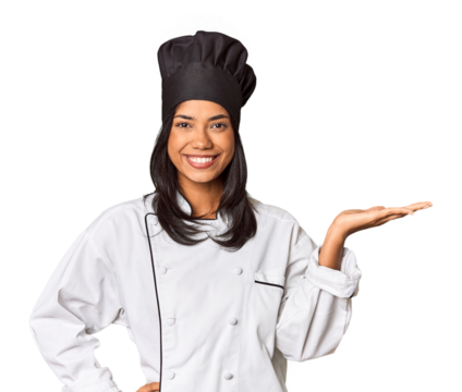 Young Filipina chef with cooking hat in studio showing a copy space on a palm and holding another hand on waist.