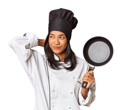 Young Filipina chef holding pan by handle touching back of head, thinking and making a choice.