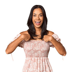 Young Filipina with long black hair in studio surprised pointing with finger, smiling broadly.