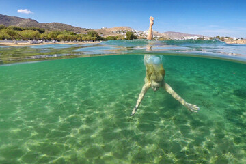 Fototapeta na wymiar Young woman swims at the bottom of the beach Livadakia on half underwater view in Serifos, Greece