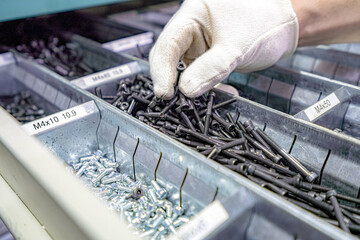 A worker selects bolts and nuts for work from a box of hardware.