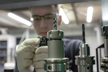 A working machine operator inspects a cutter for a CNC machine from a tool rack.