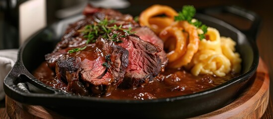 Dry aged roast beef, onion rings, and spaetzle in an iron pan with brown sauce. - obrazy, fototapety, plakaty