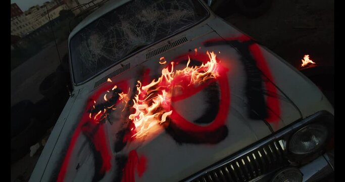 Fire dangerous burning on the destroyed with cruel old car's bonnet, painted bright red signature riot. A broken car at dawn time and flame reminding about violent street protests actions