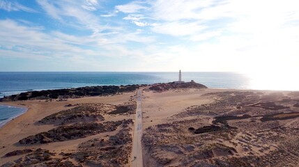 Faro de Trafalgar, aerial view of the lighthouse at a sandy headland with dunes during the sunset,...