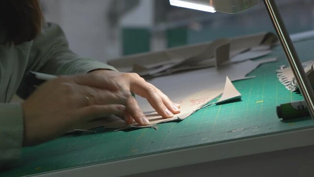 Close-up of a shoemaker cutting pieces of leather on a table in a workshop. A female tailor traces patterns on pieces of leather and prepares blanks with a knife for making shoes. Shoe making process