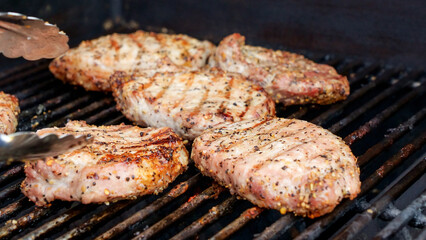 Grilled meat steak on stainless BBQ grill with flames on dark background. Food and cuisine concept.