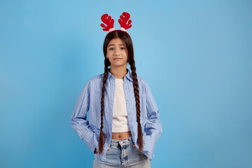 Confident teenage girl with decorative deer horns and pigtails on blue background.