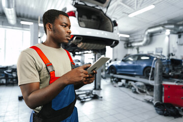 Young African auto mechanic using digital tablet in a car service