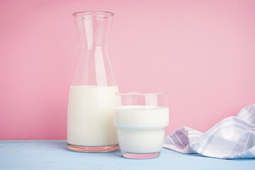 Carafe and glass of fresh milk on light pink background.